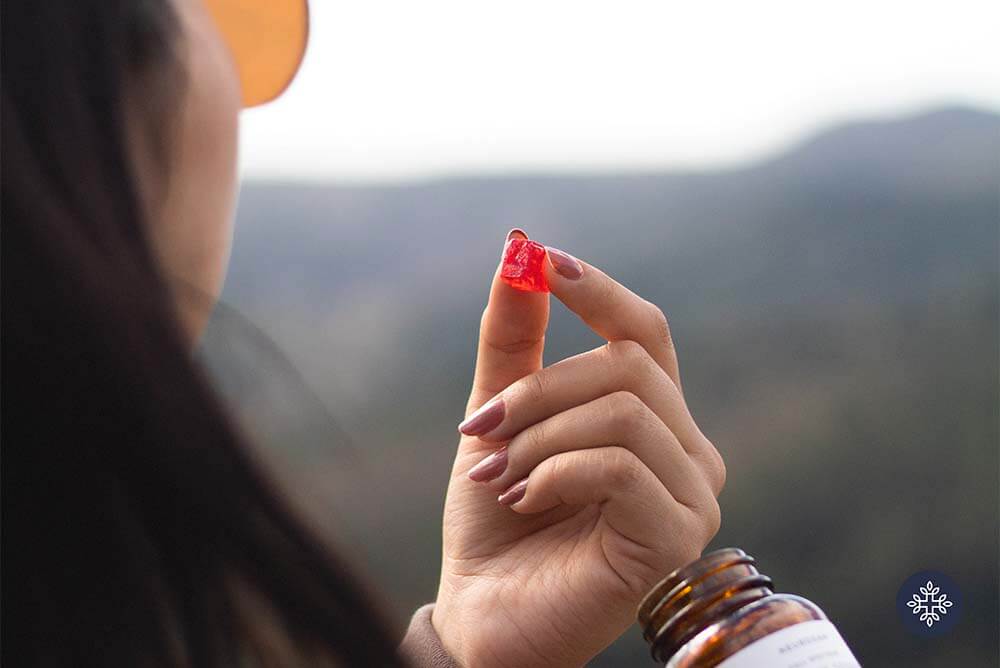 A woman holding a piece of red CBD Gummy Squares, mountain range in the background