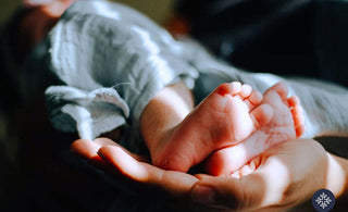 A mother holding a baby dearly with the closeup at the feet of baby laying on mother's palm