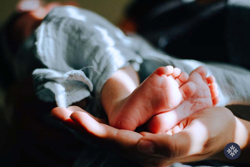 A mother holding a baby dearly with the closeup at the feet of baby laying on mother's palm