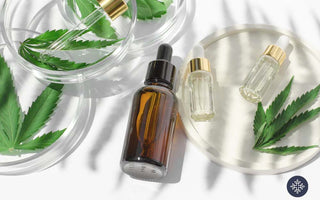 A half-filled unlabeled glass bottle laying beside hemp leaves and mini glass bottles