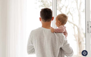 a dad holding a baby, standing near a glass door