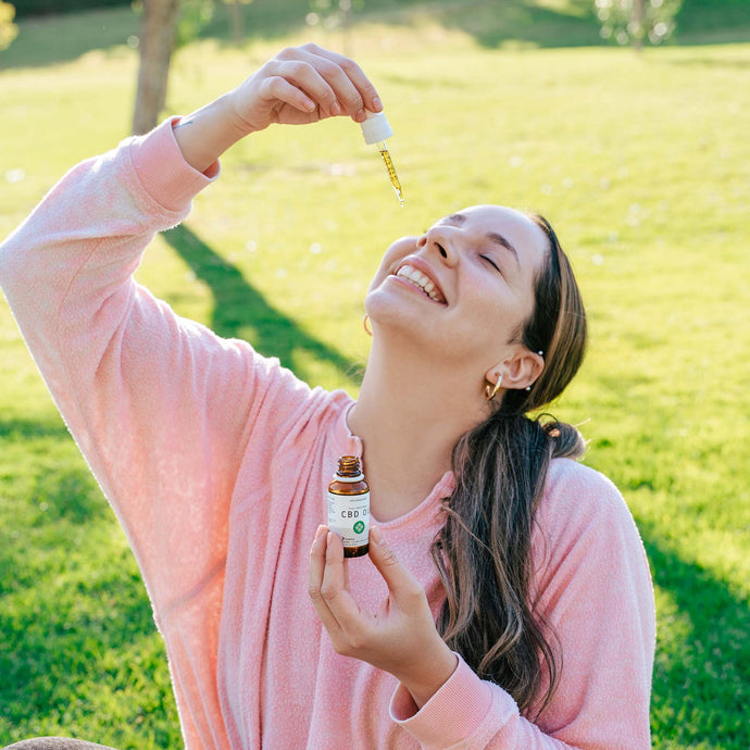  woman with blissful expression while administering CBD oil using a filled dropper into her mouth