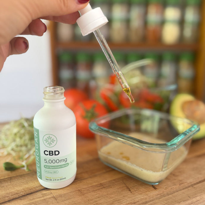 CBD oil dropper being used with a 5,000mg CBD bottle, surrounded by fresh ingredients.