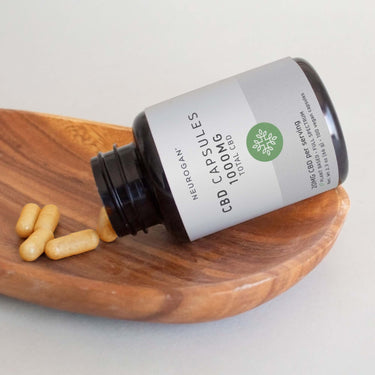 An open bottle of CBD capsules lying with four capsules poured onto a wooden plate.