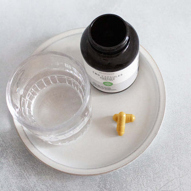 two piece of CBD capsules in a plate beside a glass of water and an open bottle of CBD capsules