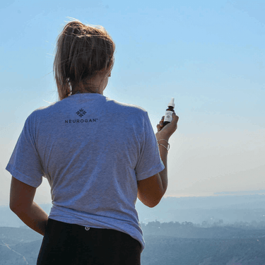 a woman holding a bottle of CBD Oil on a relaxing mountain scenery