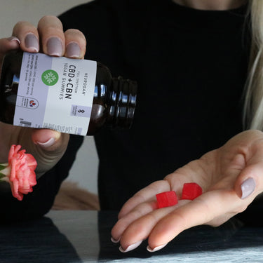 Woman pouring into her hand 2 red gummy squares from a bottle of CBN Vegan Gummies. 