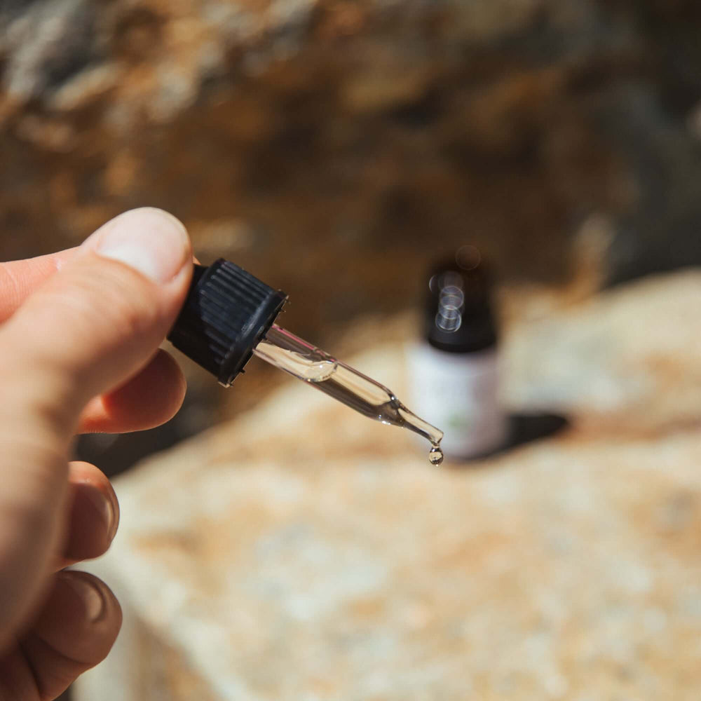 Handheld close up of free CBD sample dropper top, with the bottle placed on a rock