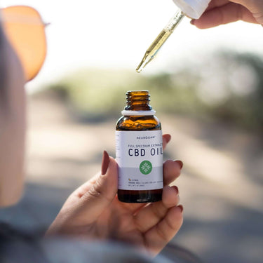 A woman holding a bottle of CBD oil and filling her CBD oil dropper