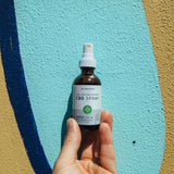 Handheld bottle of CBD spray against a blue painted wall.