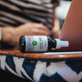 A CBD spray bottle lying on a laptop table next to a working person.