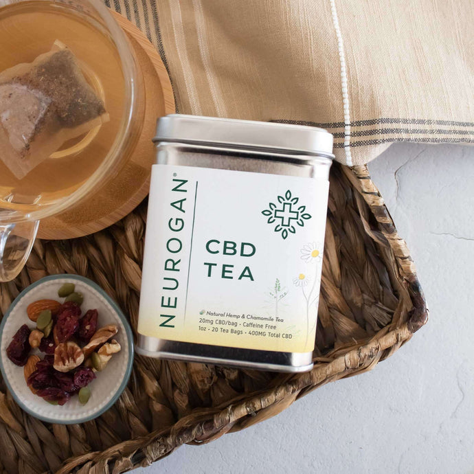 A brewing CBD tea on clear cup beside a serving of mix nuts and the box of tea on a wooden board