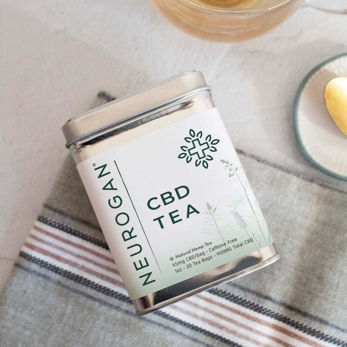 A pack of CBD tea laying on a handkerchief on a table beside a teaspoon