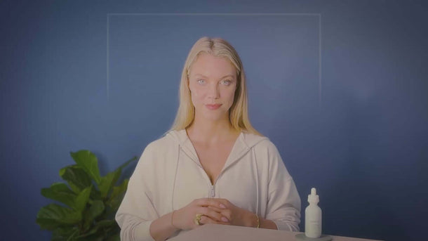 Young woman showcasing a CBD tincture bottle against a blue background, promoting natural wellness.