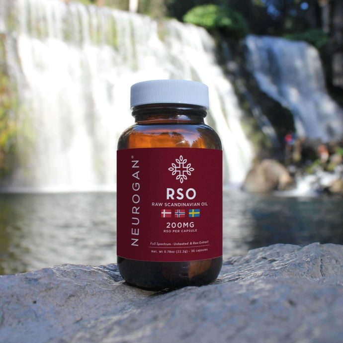 A bottle of RSO capsules on a rock with a relaxing waterfall scenery at the background