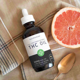 A bottle of THC oil laying on a handkerchief beside a sliced citrus fruit and a spoon