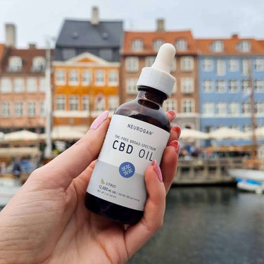 Close up of hand holding a bottle of THC-Free CBD Oil, colored Scandinavian houses in the background