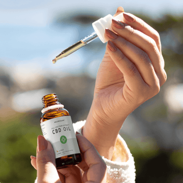 Hand holding marked dropper filled with CBD oil and a bottle of Full Spectrum CBD Oil