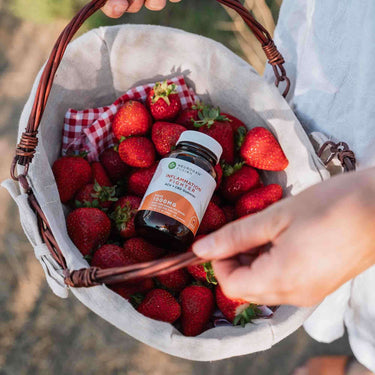 Person holding a wooden basket with strawberries and a bottle of CBD + ACV Vegan Gummies in it