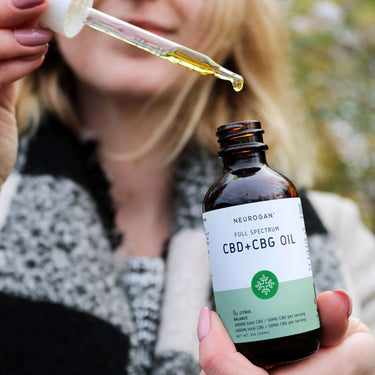 Close up of CBD + CBG oil bottle with a woman holding the half-filled dropper