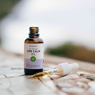 An open bottle of CBN calm oil on a wooden table with the dropper laying beside it