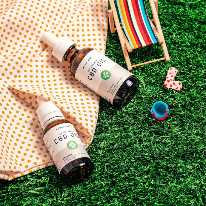Two bottles of CBD Oil 2000MG, laying on orange polka dotted picnic blanket & grass lawn with beach accessories