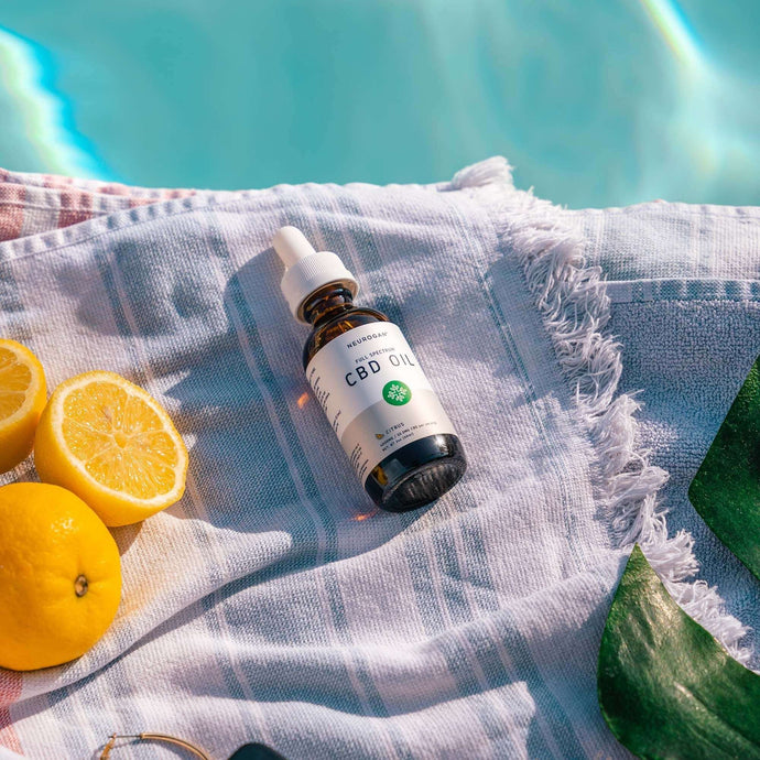 Sunlit bottle of CBD oil next to oranges on a swimming towel