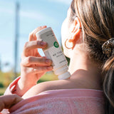 CBD Roll On being applied to the shoulder of a woman standing outside in sunlight