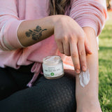 woman wearing a pink sweater with sleeves rolled up, applying CBD Cooling Rub onto arm