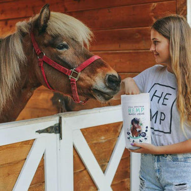 Woman scooping CBD Horse Chews full spectrum from the bag to feed to the horse beside her