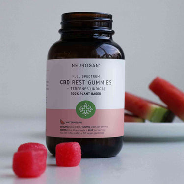 A bottle of CBD Rest Gummies with3 pieces out of the bottle and slices of watermelon at the back
